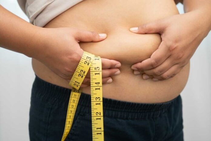 Asian,Woman,With,Fat,Belly,Big,Size,Overweight,And,Obesity Person pinching belly fat while holding a yellow measuring tape