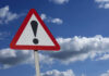 Warning sign with exclamation mark against sky