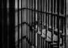Chaos Erupts Inside Prison Rusty prison cell bars in dim lighting.