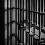 Chaos Erupts Inside Prison Rusty prison cell bars in dim lighting.