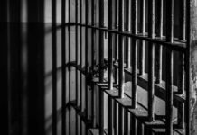 Chaos Erupts Inside Prison Rusty prison cell bars in dim lighting.