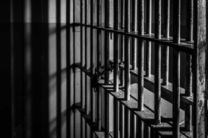shutterstock_7243457533 Rusty prison cell bars in dim lighting.
